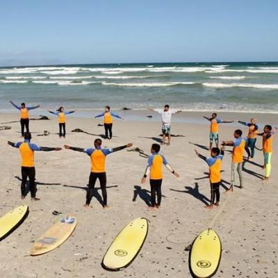 Niños aprenden ejercicios de calentamiento durante el voluntariado de surf en Sudáfrica. Voluntarios enseñando a surfear a niños de Sudáfrica.